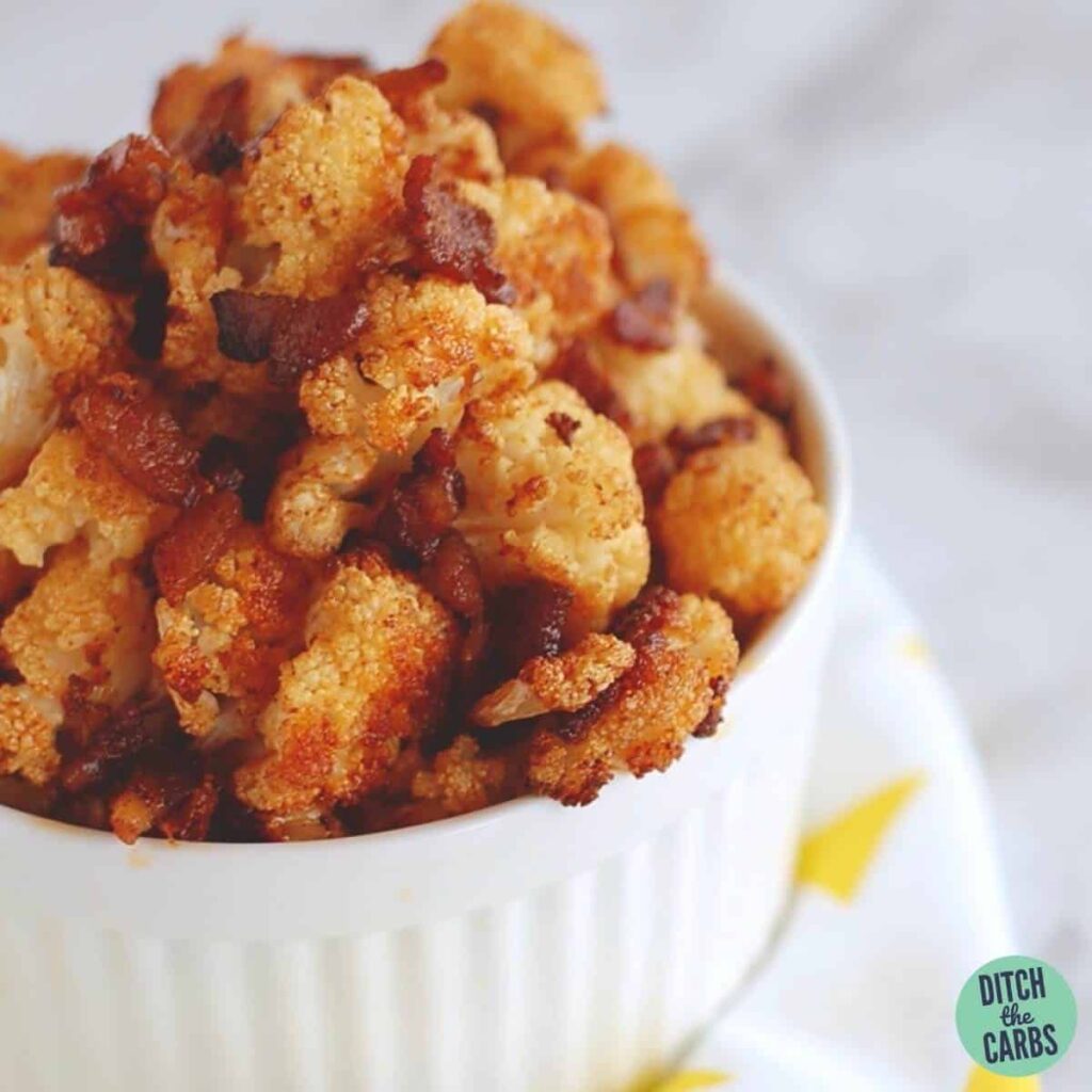 closeup of bacon cauliflower in a white ramekin bowl on a white napkin with yellow triangles