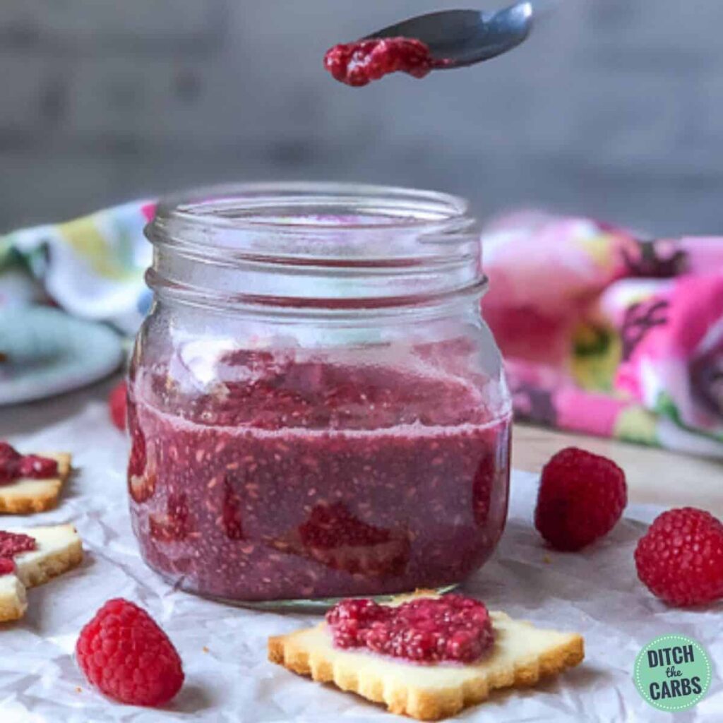 Spoon lifting raspberry jam from the glass jar